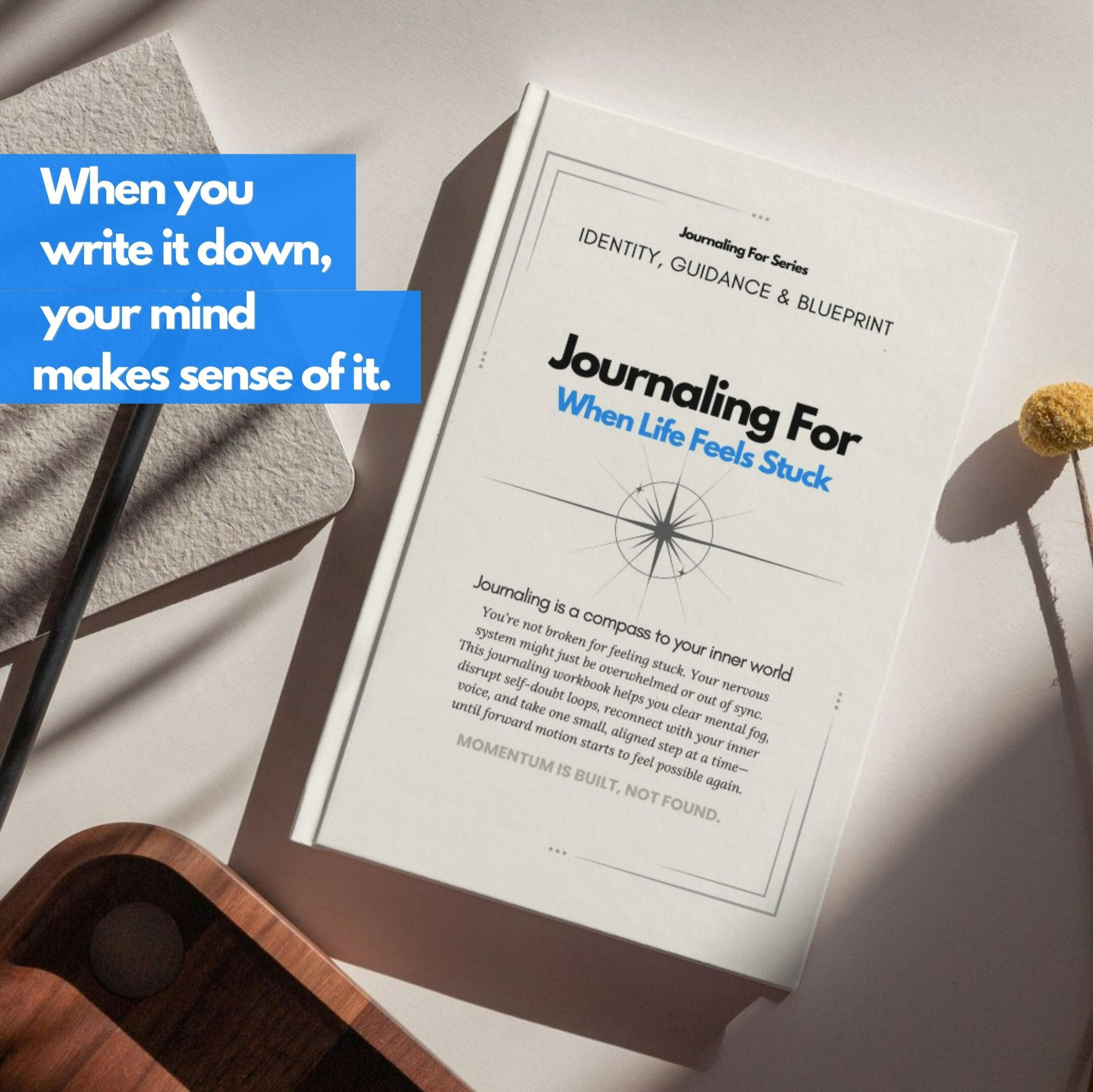 Journaling For – When Life Feels Stuck’ workbook of the Identity, Guidance & Blueprint category placed on a light wooden surface beside a notebook, a stone, and a small yellow flower, with a blue overlay that reads ‘When you write it down, your mind makes
