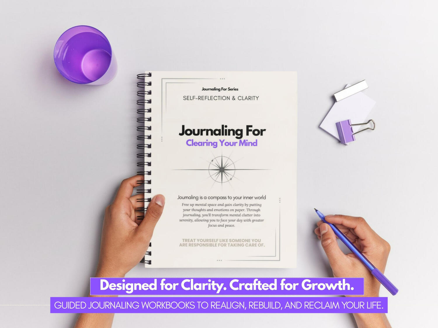 “Journaling For – Clearing Your Mind’ spiral-bound workbook held by a person over a minimalist desk with purple stationery accents.