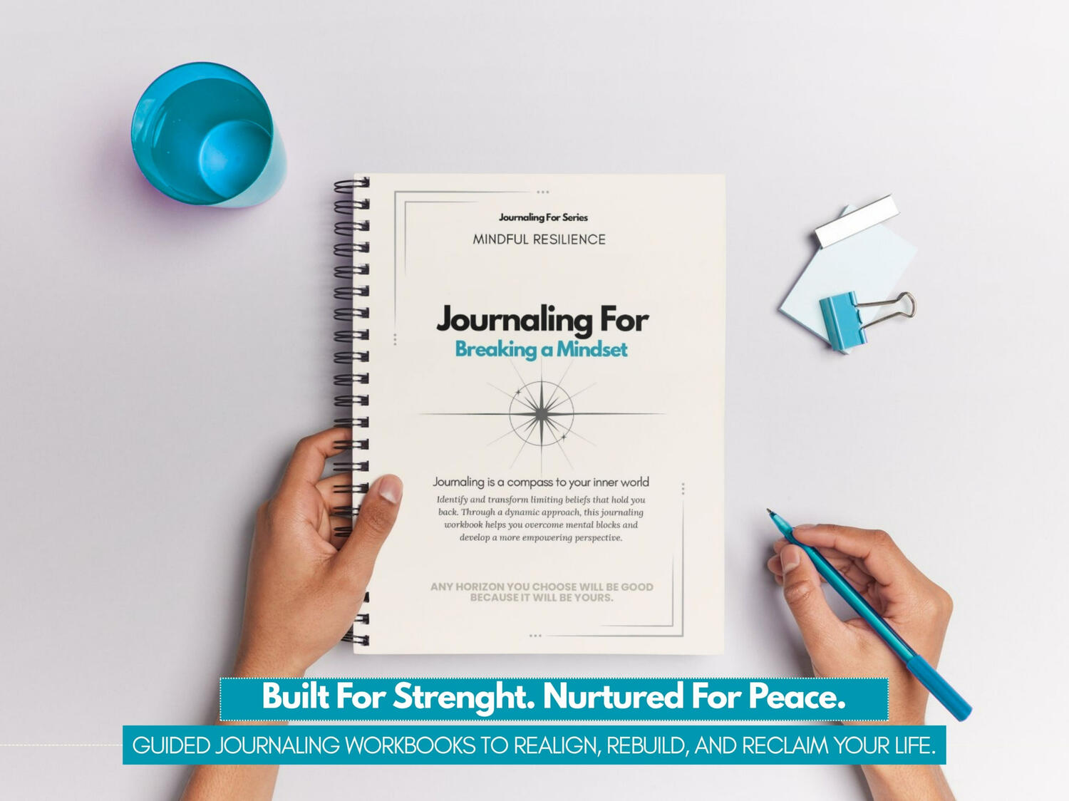 Journaling For | Breaking a Mindset Journaling For – Breaking a Mindset’ spiral-bound workbook held by a person on a clean white desk with teal stationery elements.